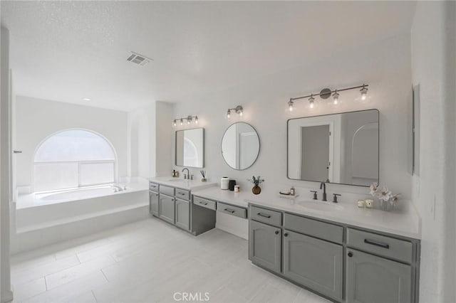 full bath with double vanity, visible vents, a garden tub, and a sink