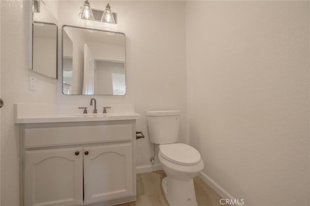 half bathroom with wood finished floors, vanity, toilet, and baseboards