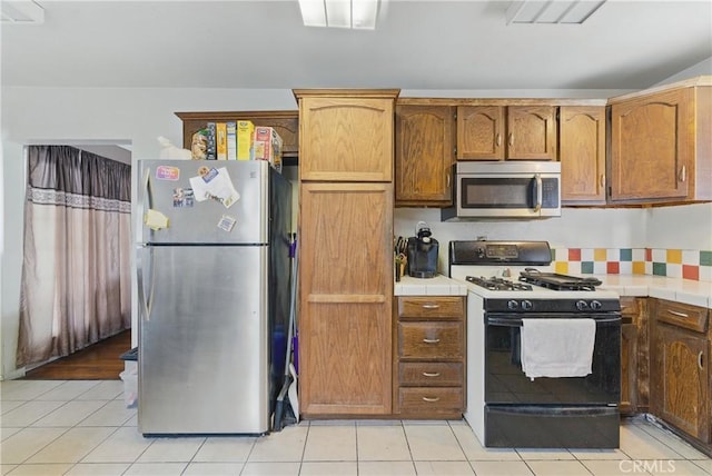 kitchen featuring brown cabinetry, tile countertops, appliances with stainless steel finishes, and light tile patterned floors
