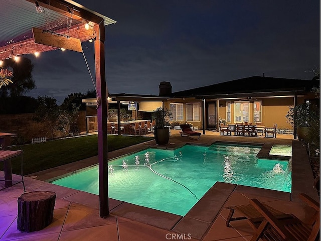pool at night with outdoor dry bar, a patio, outdoor dining space, and an outdoor pool