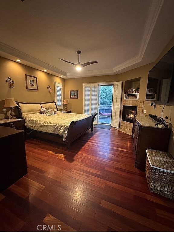 bedroom with dark wood-style floors, access to exterior, a tile fireplace, and a raised ceiling