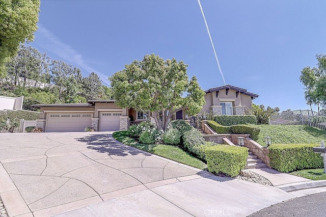 view of front of home with a garage, driveway, stone siding, stucco siding, and fence