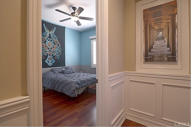 bedroom featuring a wainscoted wall, a ceiling fan, and dark wood finished floors