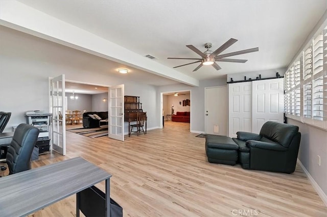living room with visible vents, a barn door, baseboards, light wood finished floors, and a ceiling fan