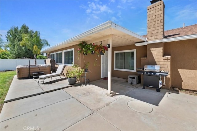 rear view of property with a patio, a chimney, stucco siding, and a hot tub