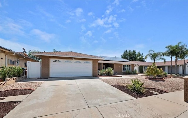 ranch-style house featuring concrete driveway, solar panels, an attached garage, and brick siding