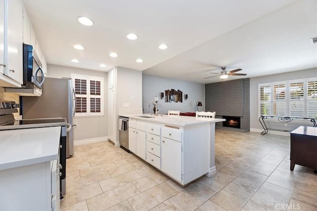 kitchen with a sink, stainless steel appliances, a ceiling fan, a peninsula, and light countertops