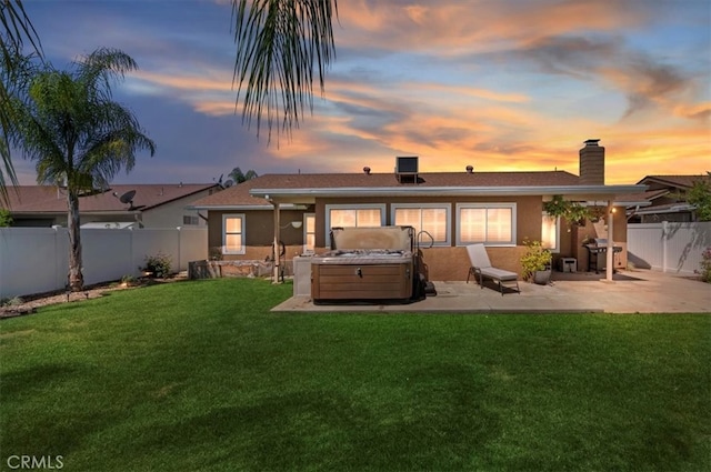 rear view of house featuring a patio, a chimney, a hot tub, a yard, and a fenced backyard
