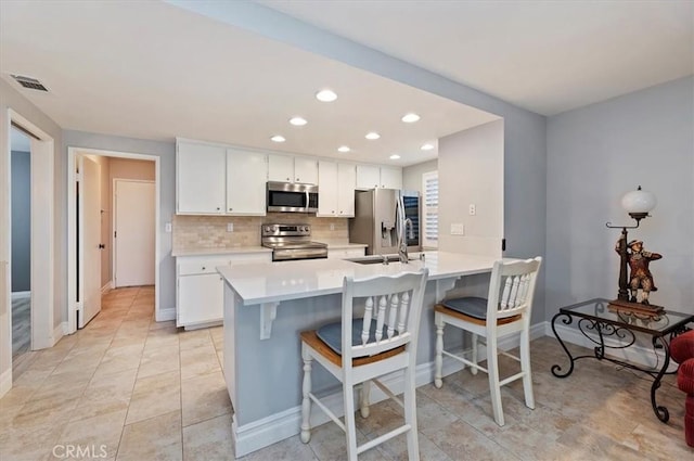 kitchen featuring decorative backsplash, a breakfast bar area, appliances with stainless steel finishes, light countertops, and visible vents