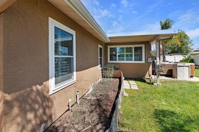 view of side of home featuring fence, stucco siding, a garden, and a lawn