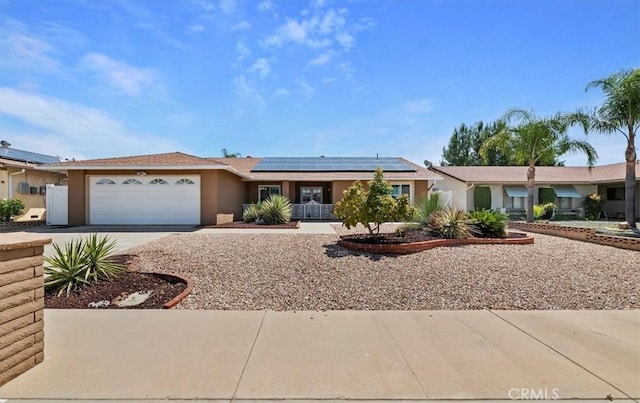 ranch-style home with brick siding, roof mounted solar panels, concrete driveway, and an attached garage