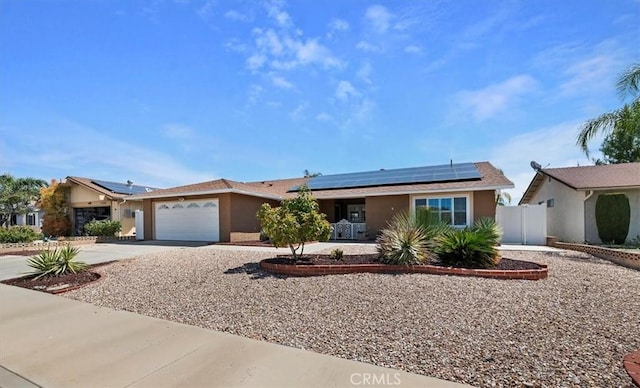 ranch-style house featuring roof mounted solar panels, concrete driveway, an attached garage, and fence