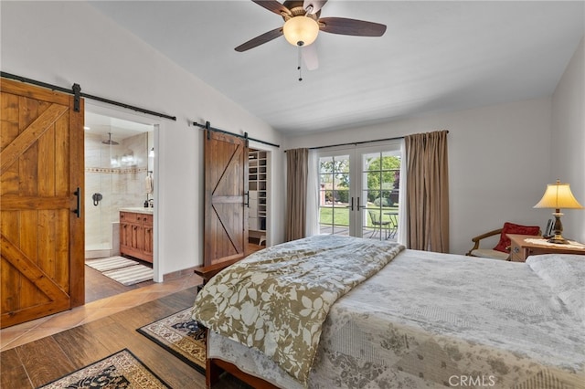 bedroom with wood finished floors, a barn door, access to outside, ensuite bathroom, and lofted ceiling