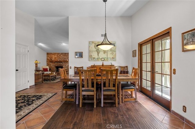 tiled dining area featuring french doors, a high ceiling, baseboards, and a brick fireplace