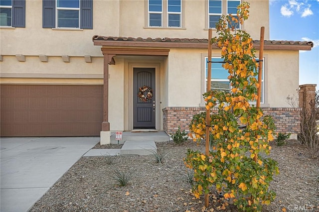 property entrance with a garage, stucco siding, a tile roof, and concrete driveway