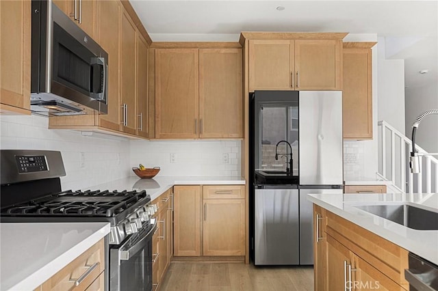 kitchen with a sink, light wood-style flooring, backsplash, light countertops, and appliances with stainless steel finishes