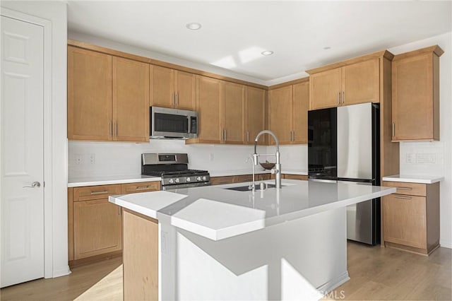 kitchen with a sink, light wood-style floors, stainless steel appliances, light countertops, and an island with sink