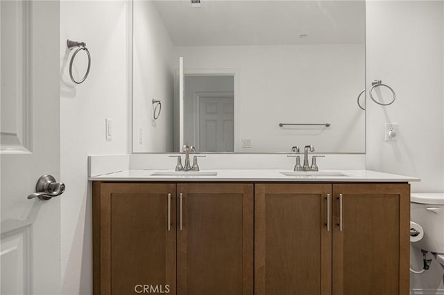 full bath with toilet, double vanity, and a sink
