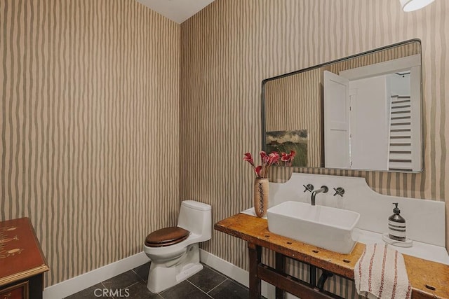 half bathroom with toilet, baseboards, wallpapered walls, tile patterned floors, and a sink