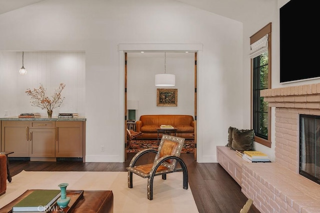 interior space featuring baseboards, dark wood finished floors, a brick fireplace, and vaulted ceiling