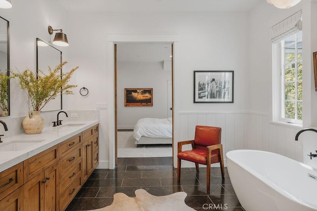 ensuite bathroom featuring a sink, a wainscoted wall, and a healthy amount of sunlight