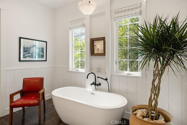 bathroom featuring plenty of natural light, wainscoting, a decorative wall, and a freestanding bath