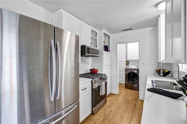 kitchen featuring light wood-style floors, washer / clothes dryer, white cabinetry, a sink, and appliances with stainless steel finishes