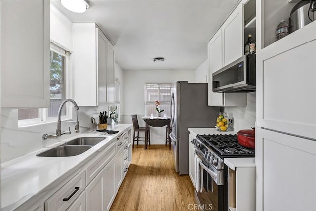 kitchen with a sink, appliances with stainless steel finishes, white cabinets, and light countertops