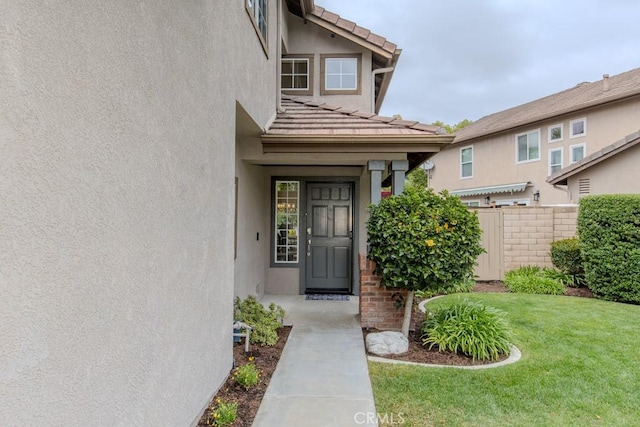 property entrance with a lawn, a tiled roof, fence, and stucco siding