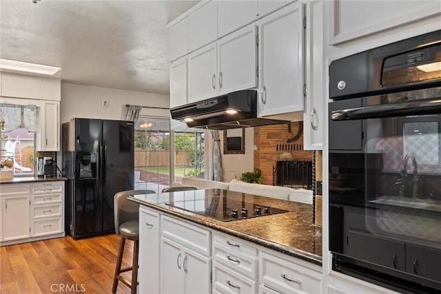 kitchen with light wood-style floors, under cabinet range hood, black appliances, dark countertops, and white cabinetry
