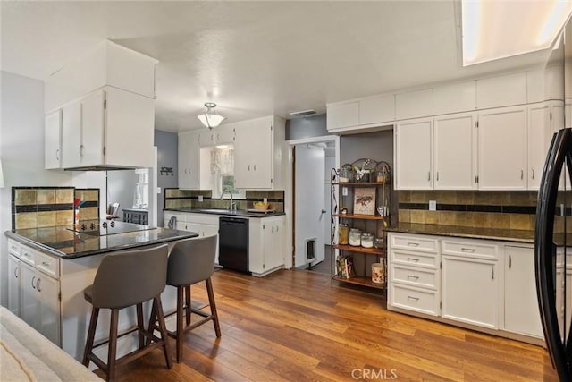 kitchen with decorative backsplash, white cabinets, dark countertops, black appliances, and wood finished floors
