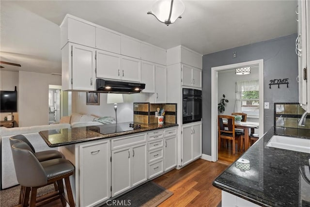 kitchen featuring under cabinet range hood, white cabinets, black appliances, a sink, and a peninsula