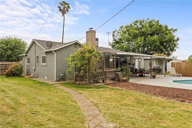 rear view of property featuring a patio, a chimney, stucco siding, a lawn, and fence