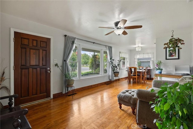living area with baseboards, wood finished floors, and a ceiling fan