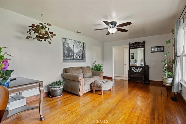 living room featuring wood finished floors, a ceiling fan, visible vents, and baseboards
