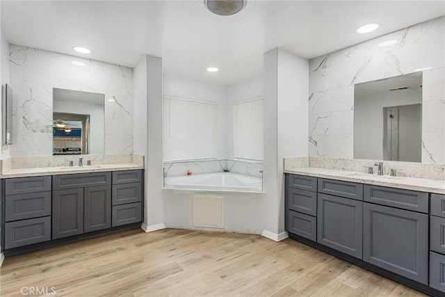 bathroom featuring two vanities, a garden tub, and a sink