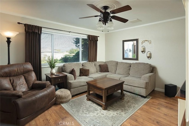 living room featuring visible vents, baseboards, light wood-type flooring, ornamental molding, and a ceiling fan