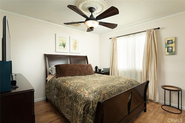 bedroom with wood finished floors, ceiling fan, ornamental molding, and baseboards