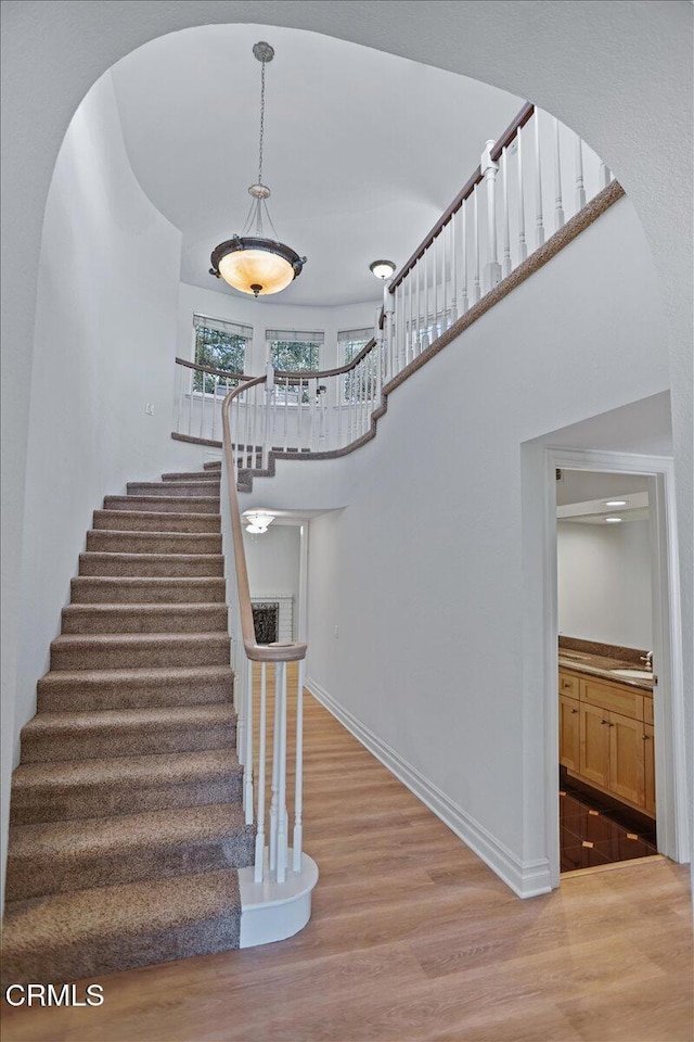 staircase with wood finished floors, arched walkways, and baseboards