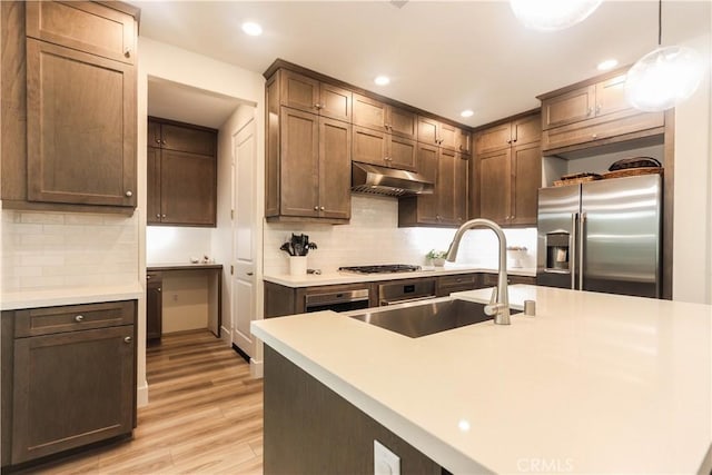 kitchen featuring a sink, under cabinet range hood, light wood-style flooring, light countertops, and appliances with stainless steel finishes