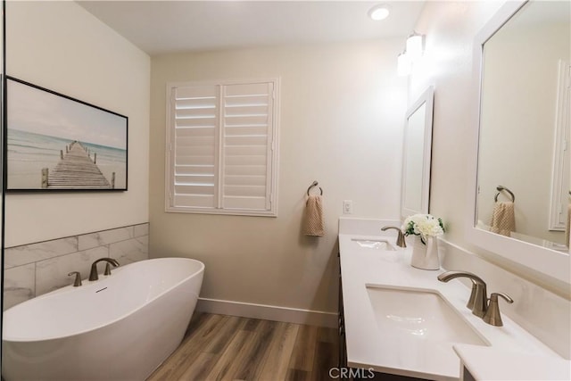 bathroom featuring double vanity, a sink, a freestanding tub, and wood finished floors