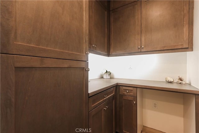 kitchen featuring built in study area, dark brown cabinets, and light countertops