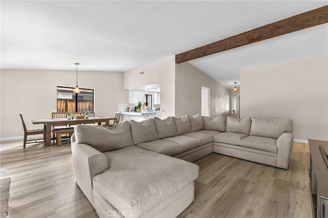 living room with visible vents, baseboards, vaulted ceiling with beams, and light wood-type flooring