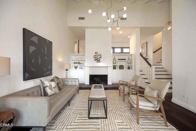 living area with stairs, visible vents, baseboards, a towering ceiling, and wood finished floors