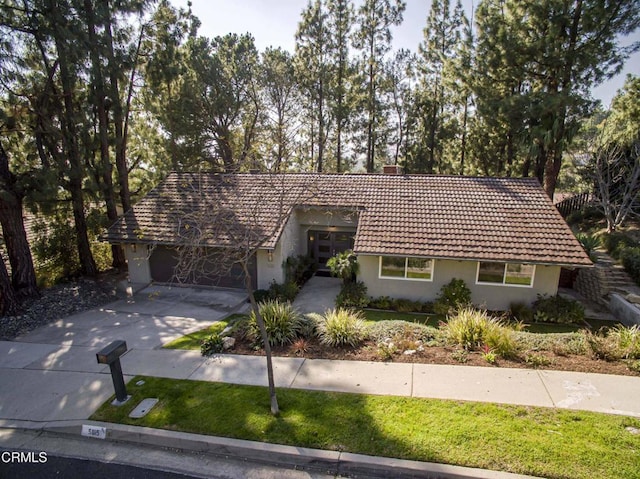 view of front of home with stucco siding, a chimney, concrete driveway, and a front lawn