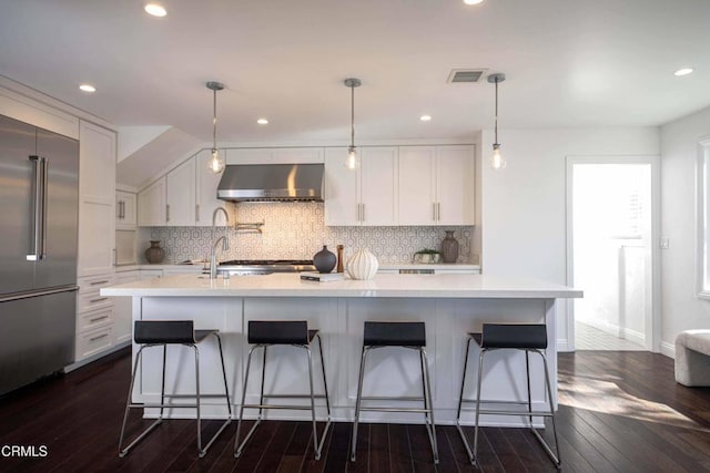 kitchen featuring white cabinets, decorative backsplash, wall chimney range hood, and built in fridge