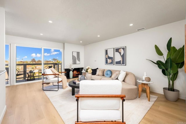 living area with recessed lighting, a warm lit fireplace, light wood finished floors, baseboards, and visible vents