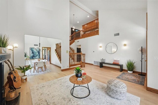 living area featuring stairs, light wood-style floors, baseboards, visible vents, and a high ceiling