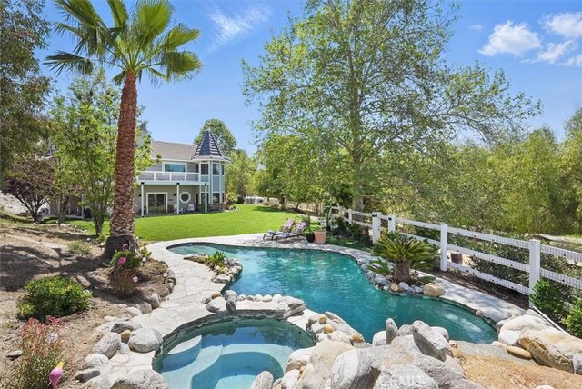 pool featuring a lawn, fence, and an in ground hot tub