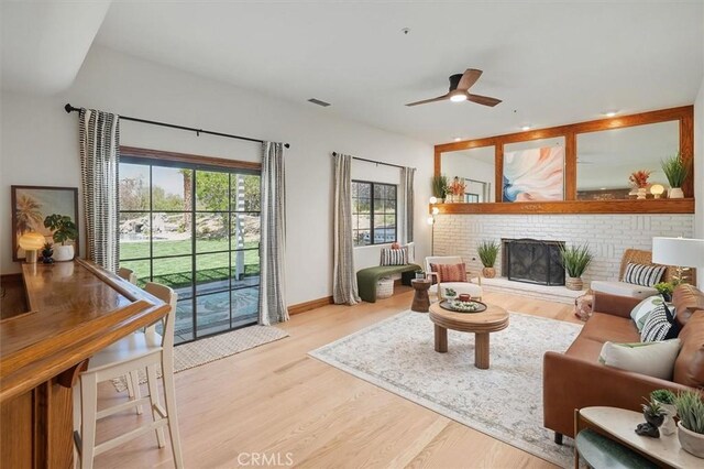 living area with visible vents, wood finished floors, ceiling fan, and a fireplace